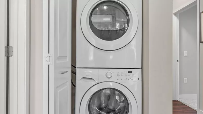 Stackable white washer and dryer unit in an open closet on dark wood floor.