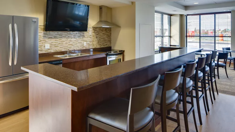 Modern kitchen with stainless steel appliances, a long bar counter with stools, and a wall-mounted TV.