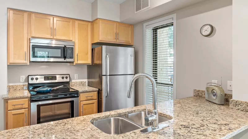 Modern kitchen with light wood cabinets, speckled granite countertops, and stainless steel appliances, including a fridge and stove.