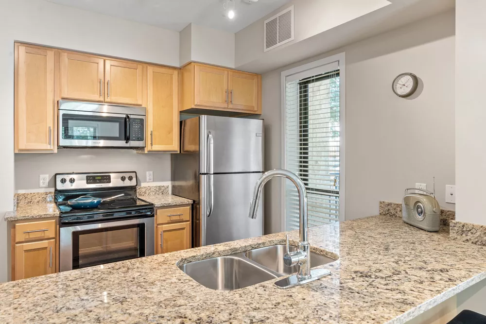 Modern kitchen with light wood cabinets, speckled granite countertops, and stainless steel appliances, including a fridge and stove.