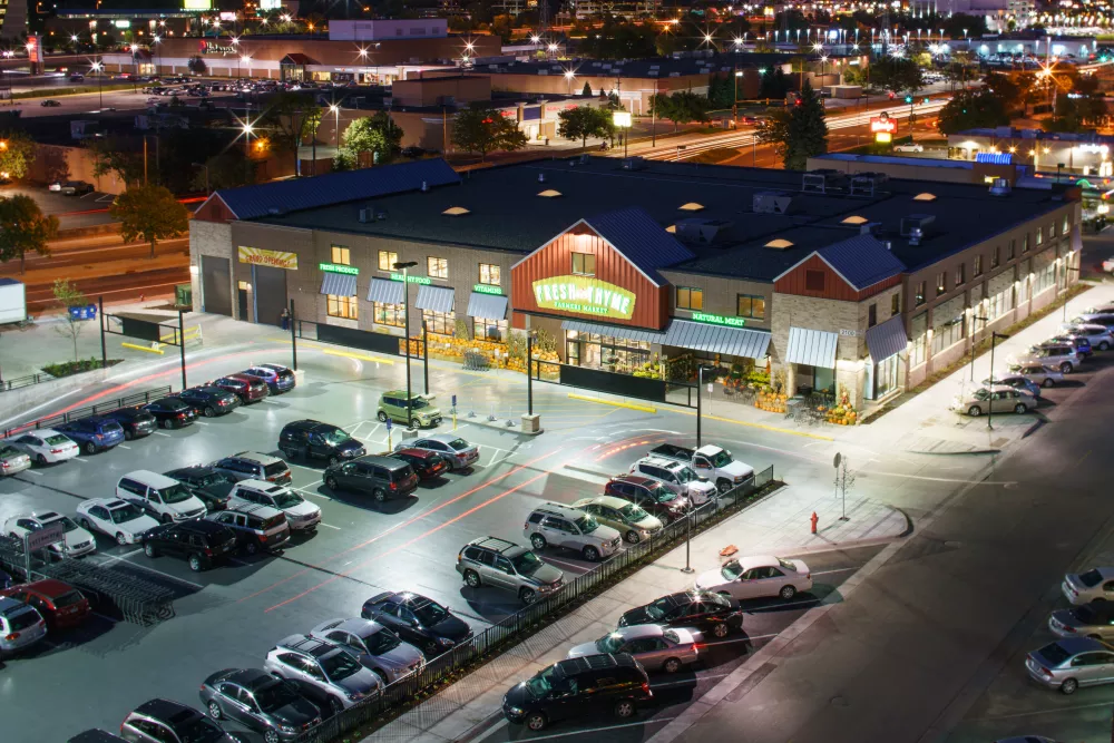 Nighttime aerial view of a brightly lit Sprouts grocery store with a large, full parking lot.